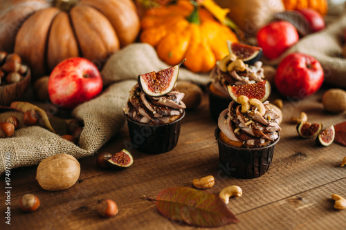 Autumn tasty cupcakes with ginger and chocolate on a wooden background of autumn harvest. Pumpkins, patsons, apples, nuts.