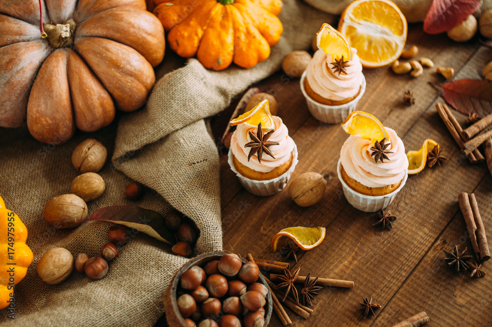 Autumn delicious cupcakes with orange and badjan on a wooden background of autumn harvest. Pumpkins, patches, apples, nuts, spices. Autumn delicious cupcakes with orange and badjan on a wooden background of autumn harvest. Pumpkins, patches, apples, nuts, spices.