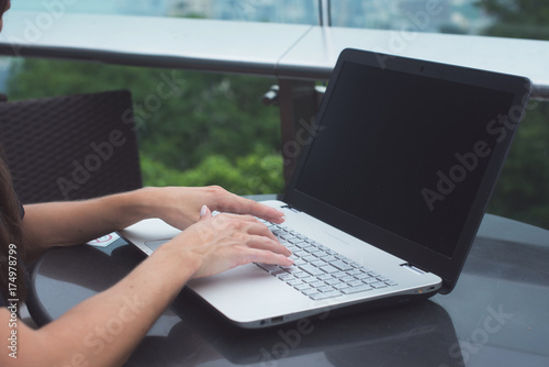 Young attractive woman typing or working on laptop sitting in rooftop cafe with city view.