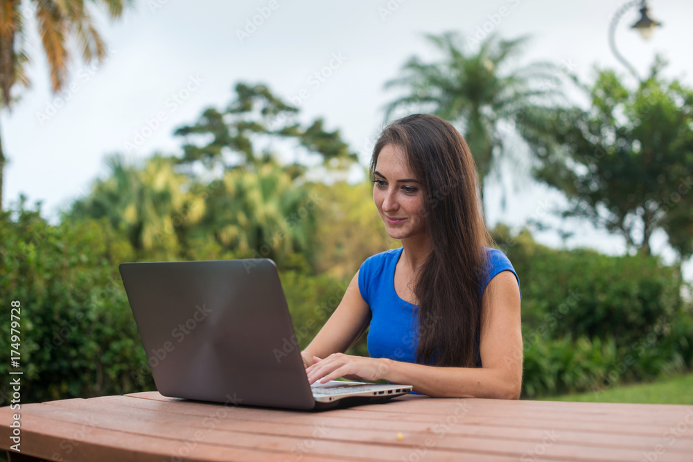 Young pretty smiling student chatting with friends on laptop in the summer park. Young pretty smiling student chatting with friends on laptop in the summer park.
