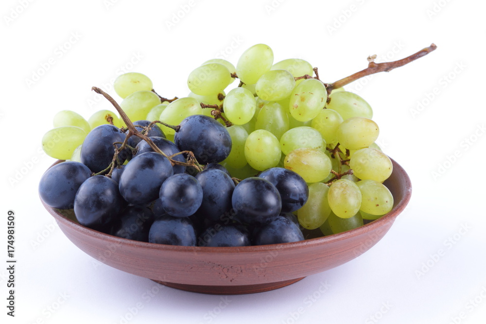 Green and blue grapes in a clay plate on a white background Green and blue grapes in a clay plate on a white background