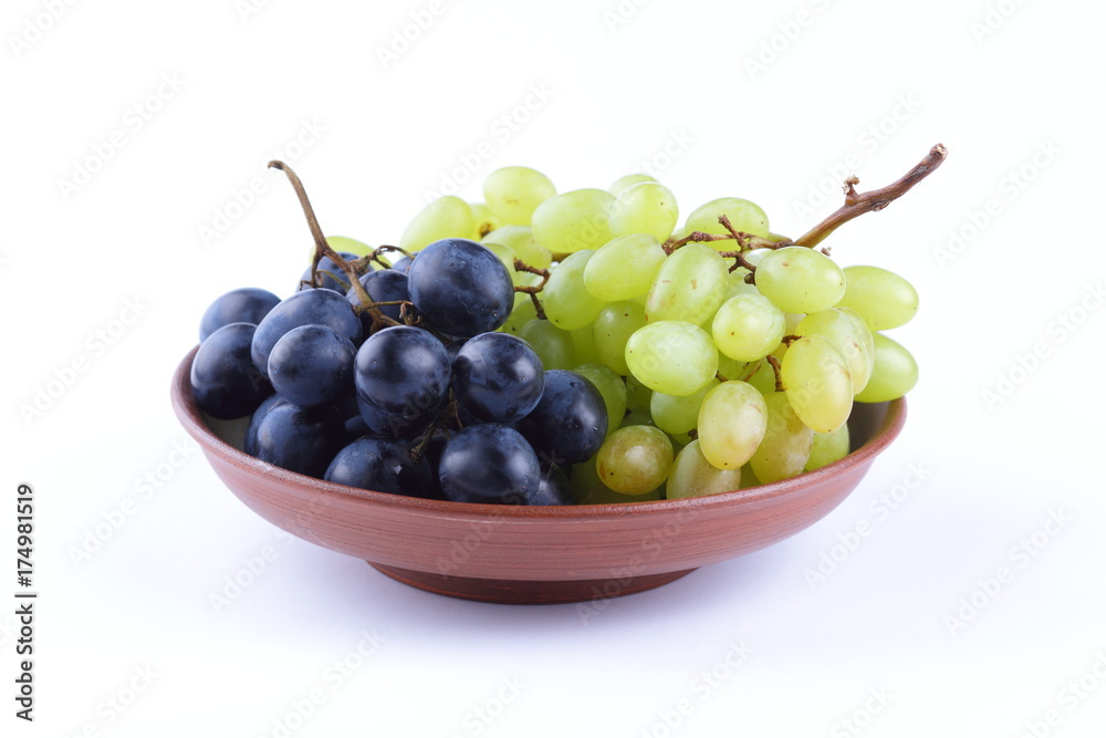 Green and blue grapes in a clay plate on a white background Green and blue grapes in a clay plate on a white background