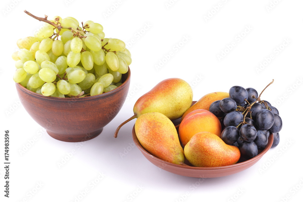 Yellow pears, green and blue grapes in a clay plate on a white background Yellow pears, green and blue grapes in a clay plate on a white background