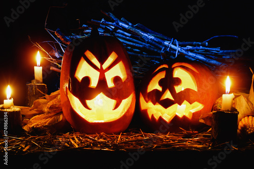 Photo for the holiday Halloween. Two evil pumpkins surrounded by candles and corn on a dark background. Image for postcard with copy space 