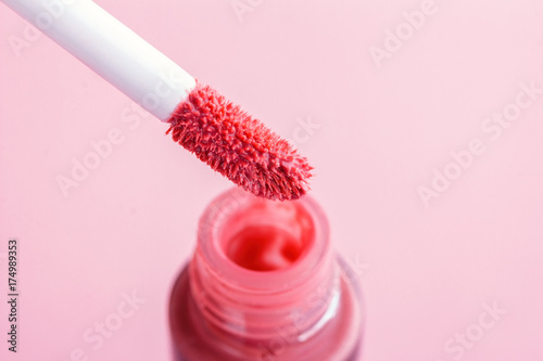 Brush for make-up lips above the bottle of liquid lipstick close-up on a pink background with copyspace
