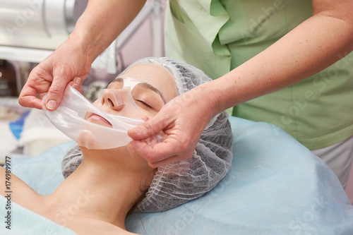 Cosmetician applying facial hydrogel mask. Customer of cosmetology clinic. photo