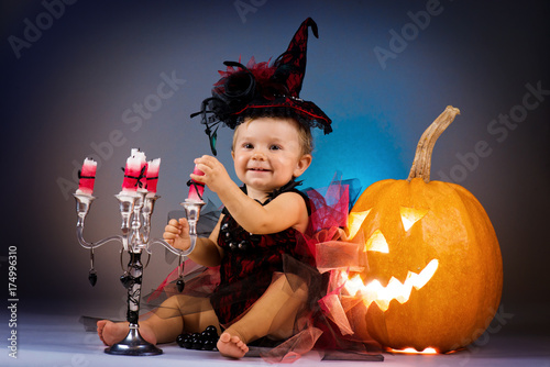 Little witch girl child laughing among pumpkins and candles.