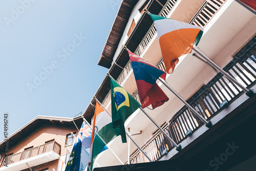 Multiple colorful national flags of different countries fixed to wooden facade of houses on sunny summer day with clear sky photo