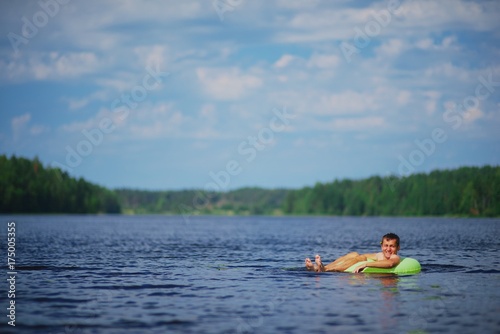 Young smiling man floating on inflatable ring in quiet calm waters on a clear Sunny day.