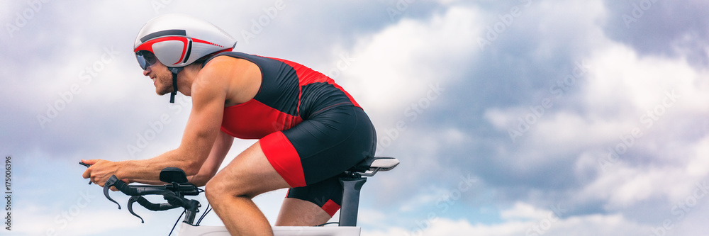 Obraz premium Triathlon biking man cycling on road bike with time trial helmet. Panorama banner crop for sky copy space.