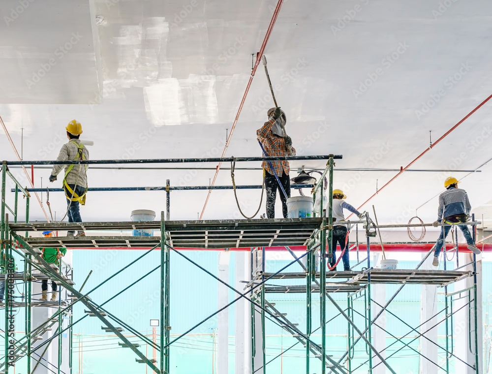 Worker man painting a gypsum plaster ceiling with paint roller on the scaffold