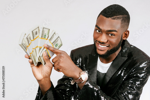 A black man looks at bundles of money. The man is holding a bundle of dollars. The man points to the dengi. photo