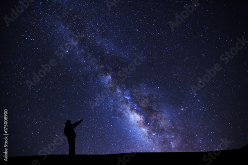 A Man is standing pointing on a bright star with milky way galaxy and space dust in the universe