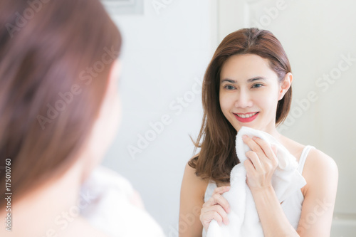 Young woman wiping her face with towel in bathroom.