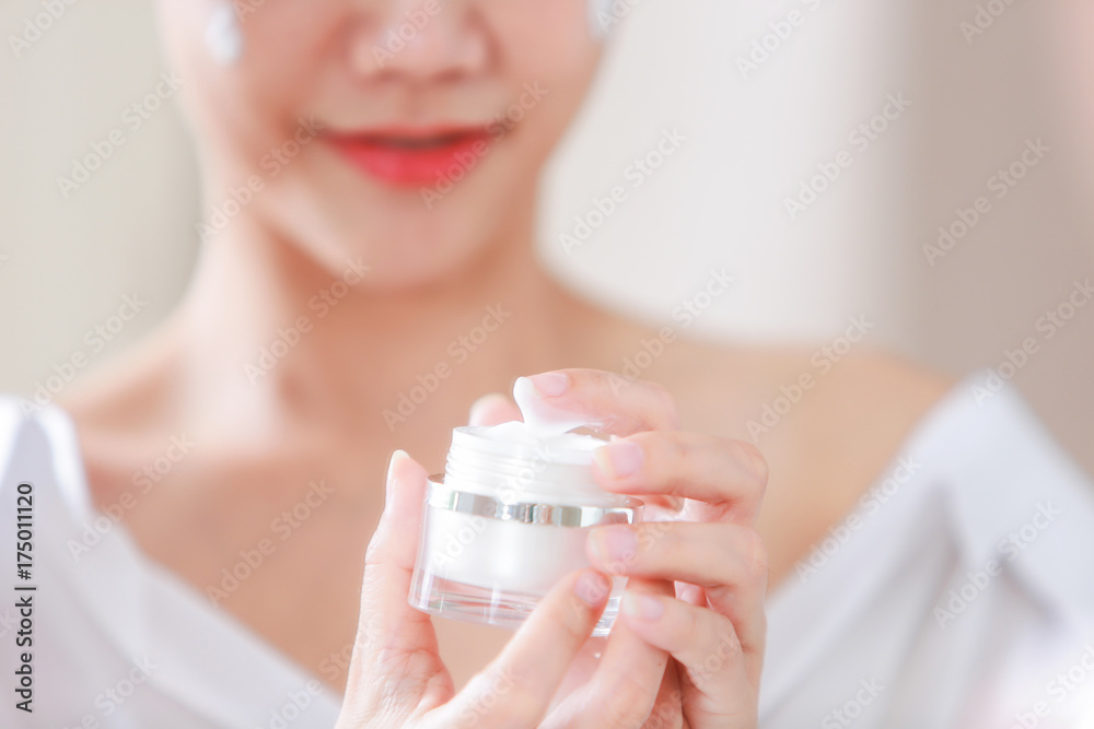 Young woman applying moisturizer on her face and holding jar of skin cream and lotion. Young woman applying moisturizer on her face and holding jar of skin cream and lotion.