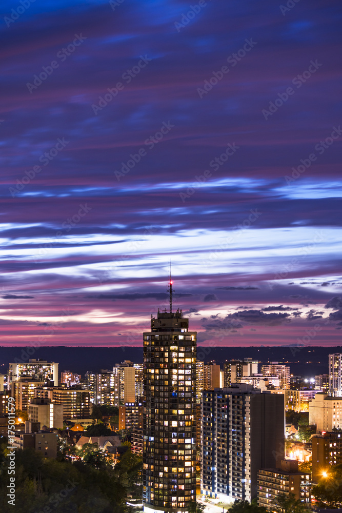 Tall building and vibrant illuminated city beneath a dark blue and pink sunset sky