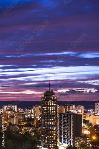 Tall building and vibrant illuminated city beneath a dark blue and pink sunset sky