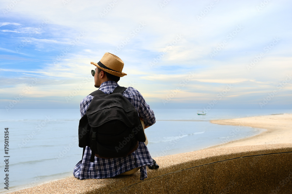 Man traveler with backpack relaxing at seaside and looking to the ocean