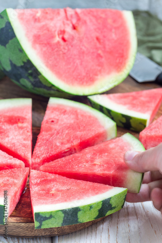 Woman hand take slice of fresh seedless watermelon cut into triangle shape laying on a wooden plate, vertical