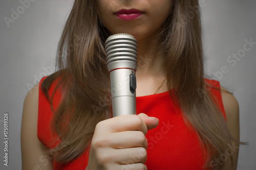 Reporter. Newscaster. Presenter. Young woman in red dress holding in hands microphone.