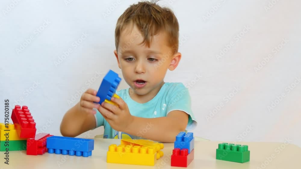 The boy collects the designer. The child builds from the colored blocks on the table. The boy collects the designer. The child builds from the colored blocks on the table.