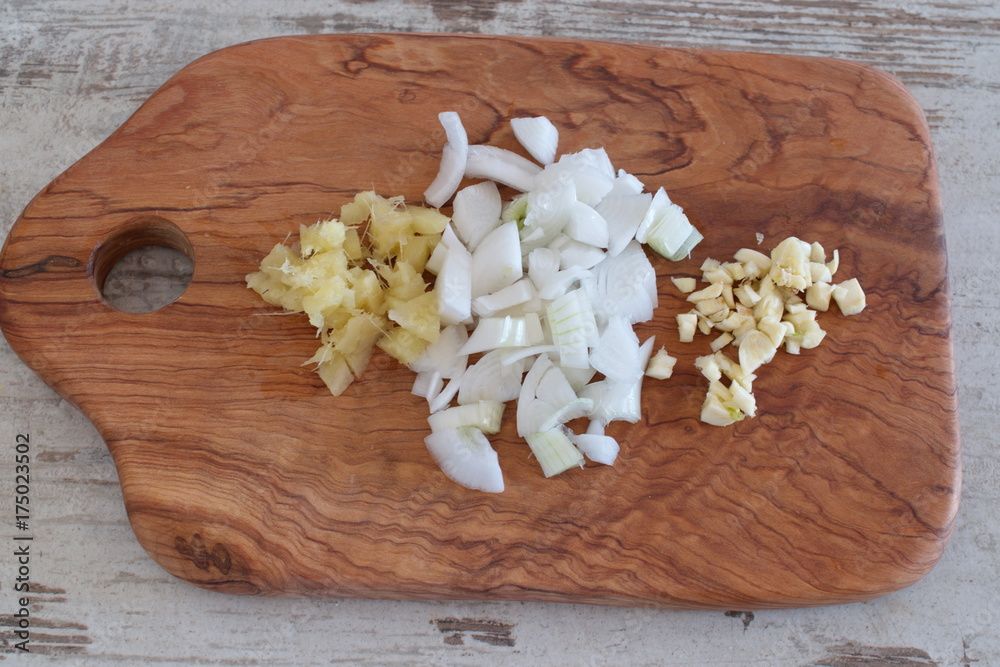 Chopped onions, ginger and garlic on an olive wooden cutting board. Chopped onions, ginger and garlic on an olive wooden cutting board.