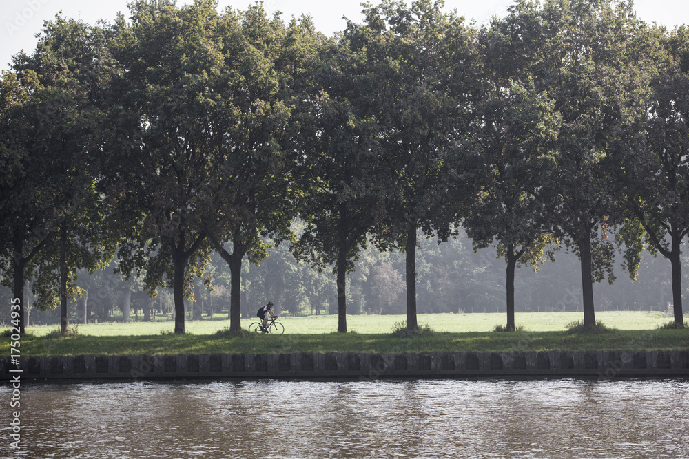 Obraz premium man on bicycle rides along amsterdam rijn kanaal in the netherlands