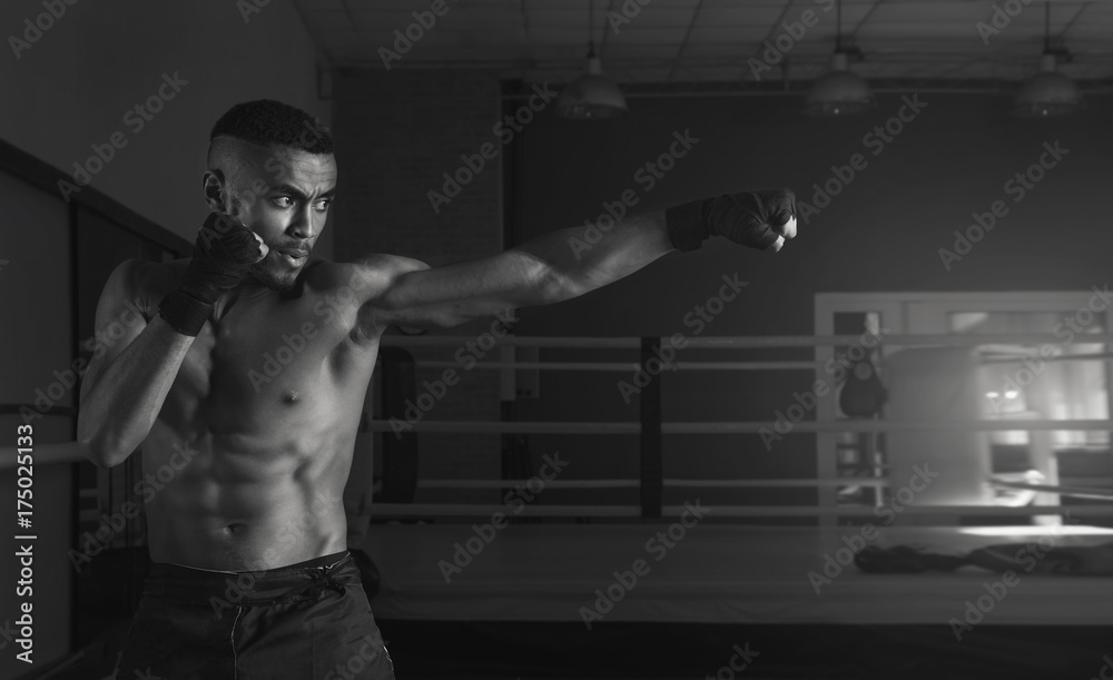 Afro american male boxer. Young man boxing workout in a fitness club. Muscular strong man on background boxing gym. Black and white photo.