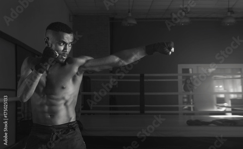 Afro american male boxer. Young man boxing workout in a fitness club. Muscular strong man on background boxing gym. Black and white photo.