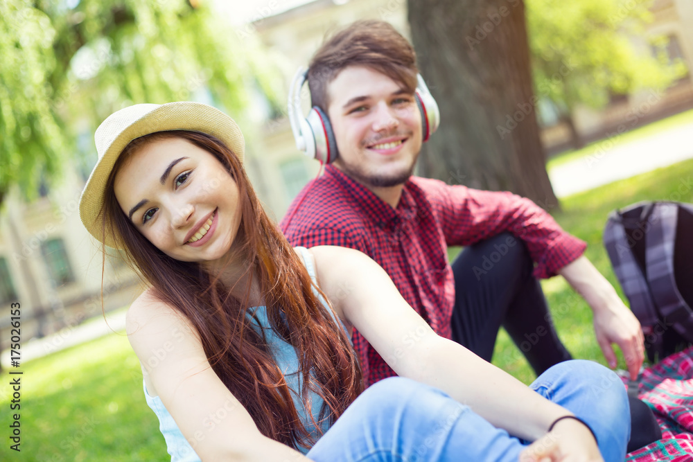 Portrait of a girl sitting next to the guy. Happy couple of young people having fun together on the green grass in the park campus. Portrait of a girl sitting next to the guy. Happy couple of young people having fun together on the green grass in the park campus.