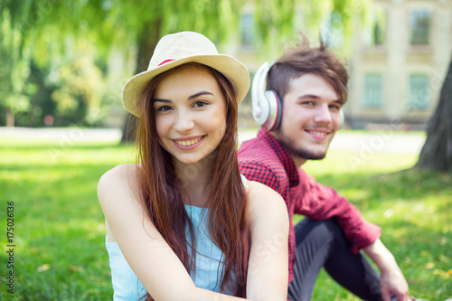 Portrait of a girl sitting next to the guy. Happy couple of young people having fun together on the green grass in the park campus. © A Stock Studio