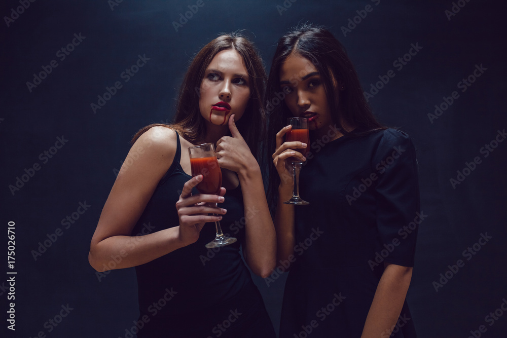 Attractive girls in the image of vampires hold glasses with blood. Halloween. Attractive girls in the image of vampires hold glasses with blood. Halloween.