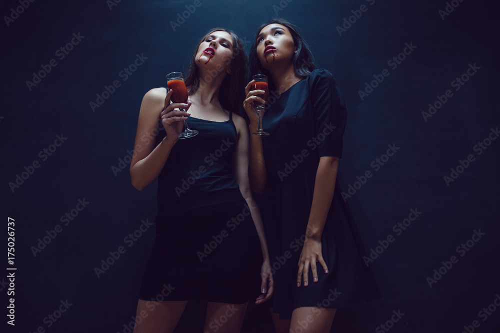 Attractive girls in the image of vampires hold glasses with blood. Halloween. Attractive girls in the image of vampires hold glasses with blood. Halloween.