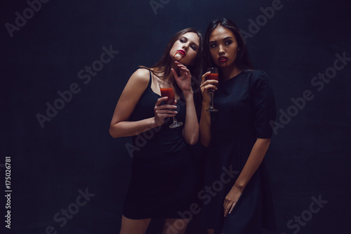 Attractive girls in the image of vampires hold glasses with blood. Halloween. photo