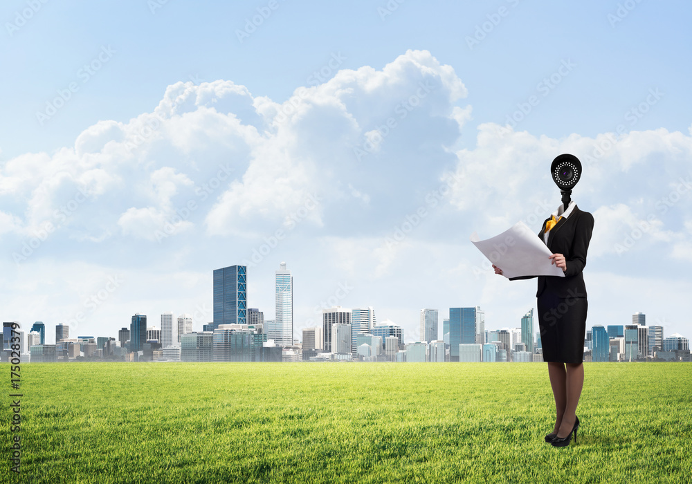 Camera headed woman standing on green grass against modern cityscape
