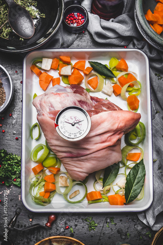 Roast pork cooking preparation on baking try with vegetables and grill timer on rustic kitchen table background, top view