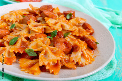 Farfalle pasta with chunks of sausage in tomato sauce on a bright background.
