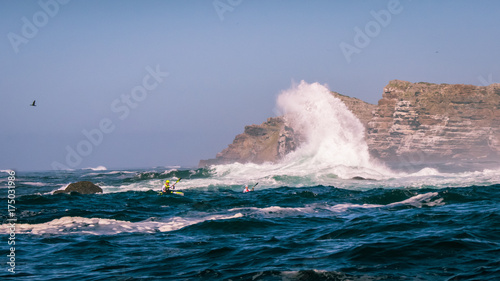 Racing Ocean Kayakers paddle their surfskis through breaking waves near the rocks