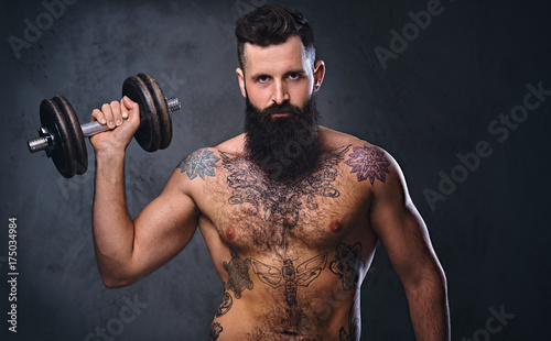 Shirtless muscular, bearded male holds dumbbell. © Fxquadro