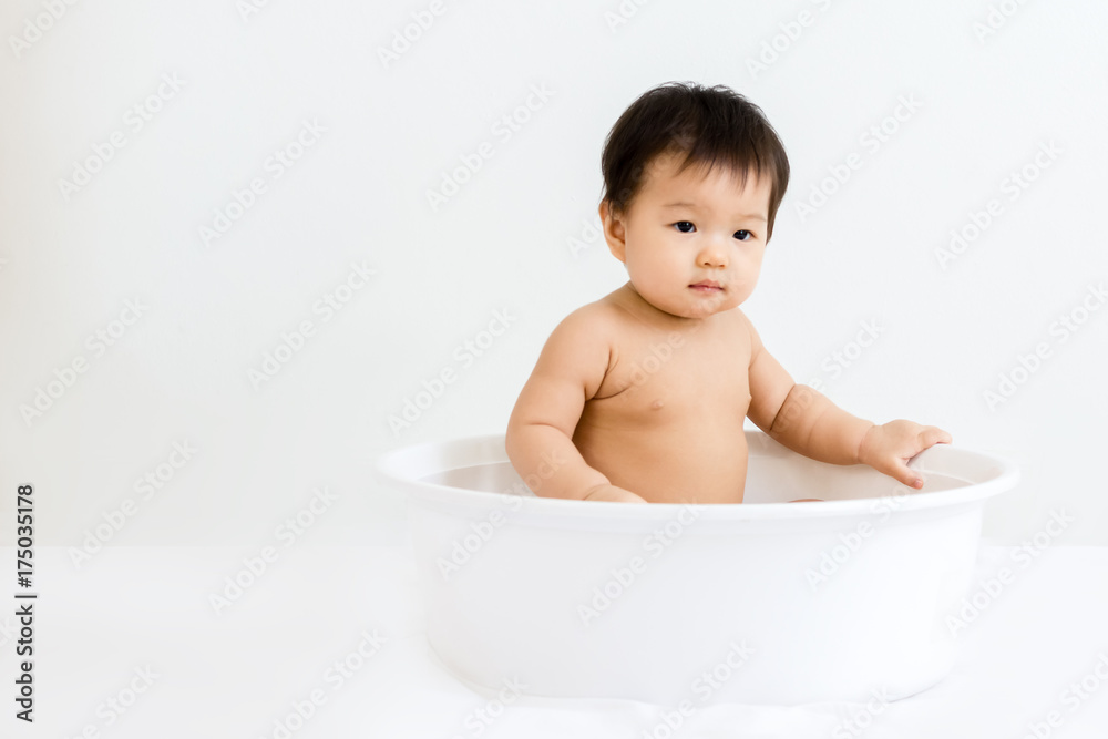 Portrait of adorable baby sitting in the basin for shower, indoors Portrait of adorable baby sitting in the basin for shower, indoors