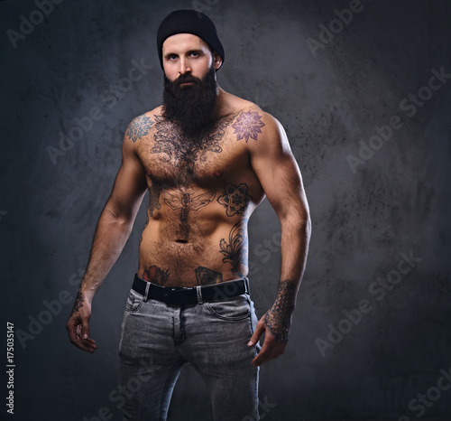 Shirtless muscular, bearded male holds dumbbell.