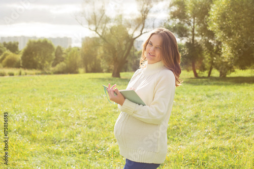 Pregnant woman walking in park sunny summer outdoor mother touching tummy writing diary notebook