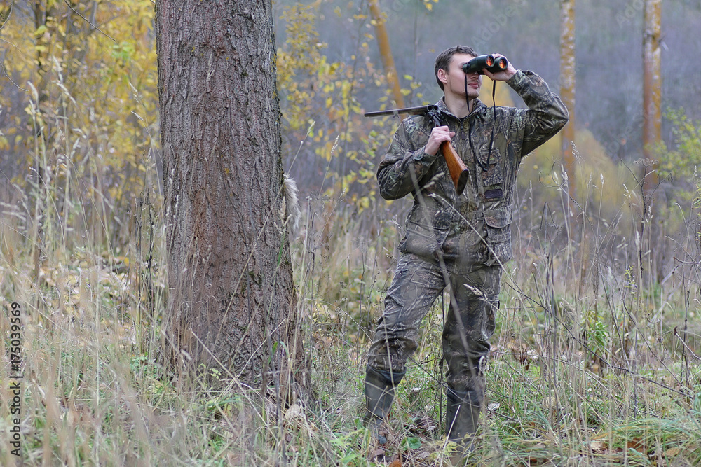 Fototapeta premium Man in camouflage and with guns in a forest belt on a spring hunt