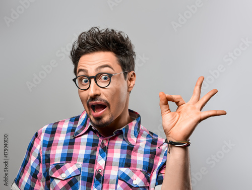 Handsome young man Having Fun Crazy. Surprised Gesturing, Open Mouth. Portrait Hipster Nerd guy in Trendy shirt, Glasses. Brunette Bearded Emotional Stylish Hairstyle on gray background. Blue Eyes