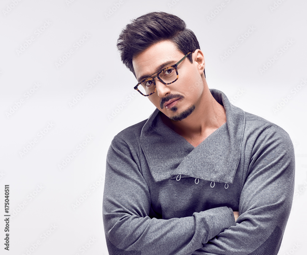 Handsome young Fashion guy. Autumn Trendy Outfit, Glasses. Sporty Confident Brunette Bearded man in fashionable gray jumper, Stylish Hairstyle. Studio fashion portrait on white background Handsome young Fashion guy. Autumn Trendy Outfit, Glasses. Sporty Confident Brunette Bearded man in fashionable gray jumper, Stylish Hairstyle. Studio fashion portrait on white background
