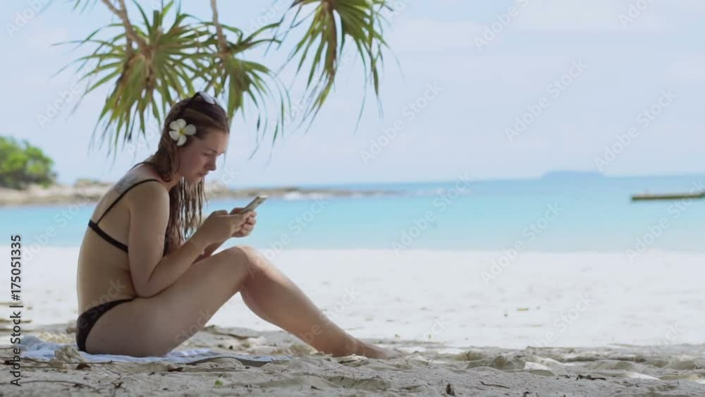 Beautiful woman using smartphone at the beach of tropical island.