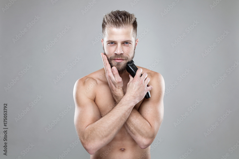 Handsome bearded man trimming his beard with a trimmer Handsome bearded man trimming his beard with a trimmer
