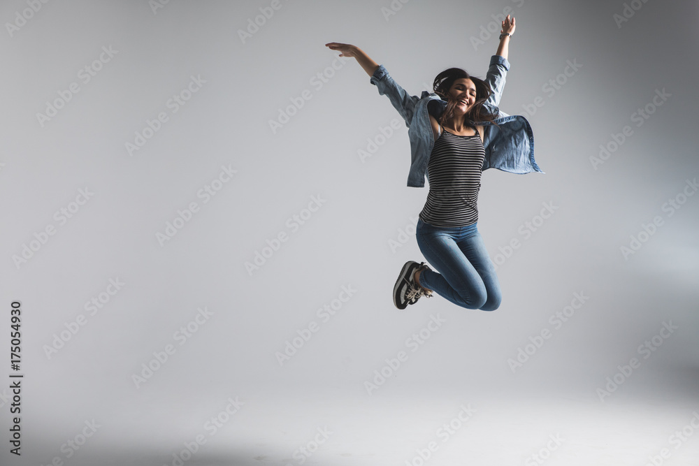 Playful young woman wearing casual jumping over grey background. Look at camera and screaming.