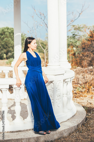 Young pretty lady in a long silk blue dress walking outdoors © Sergey