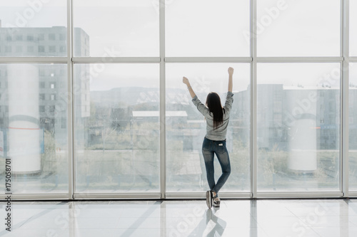 Confident woman spreading hands standing at office window, enjoying big city, successful entrepreneur celebrating business success with arms open wide, feeling powerful inspired, rear view photo